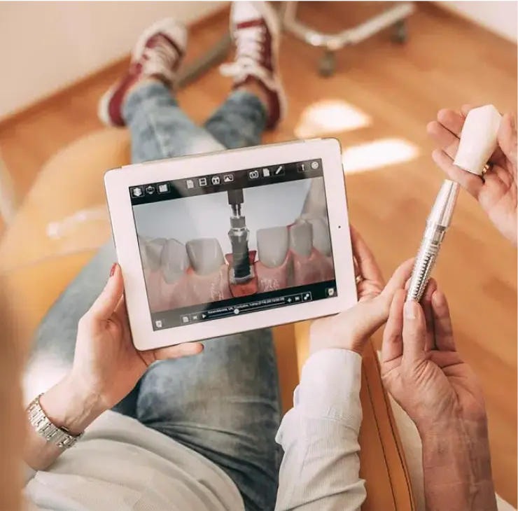 Patient hält ein Zahnimplantatmodell und betrachtet auf einem Tablet den Behandlungsprozess in der Zahnarztpraxis Sandhofpassage Frankfurt.
