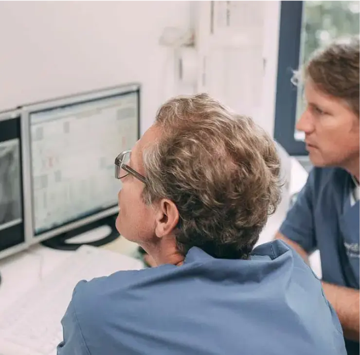 Zwei Zahnärzte bei der Analyse von Röntgenbildern auf dem Monitor während der Implantatplanung in der Zahnarztpraxis in Bad Soden.